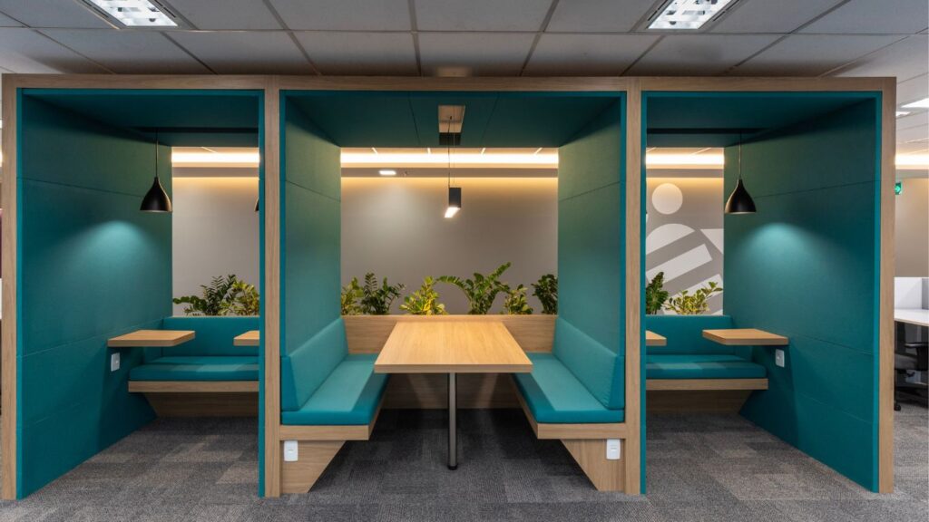 Foto de cabine privativa de trabalho. Sao 3 núcleos, divididos por paredes. Os núcleo contém bancos e mesas.